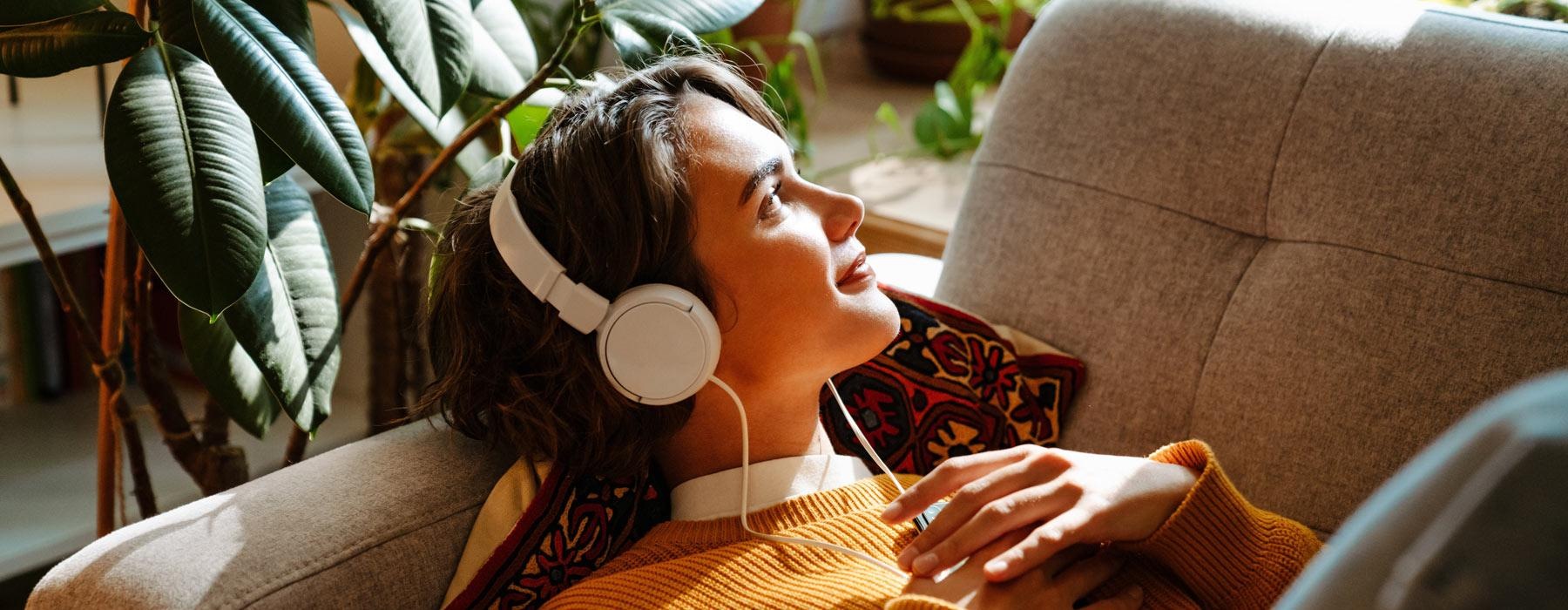 woman lies on her couch listening to her headphones