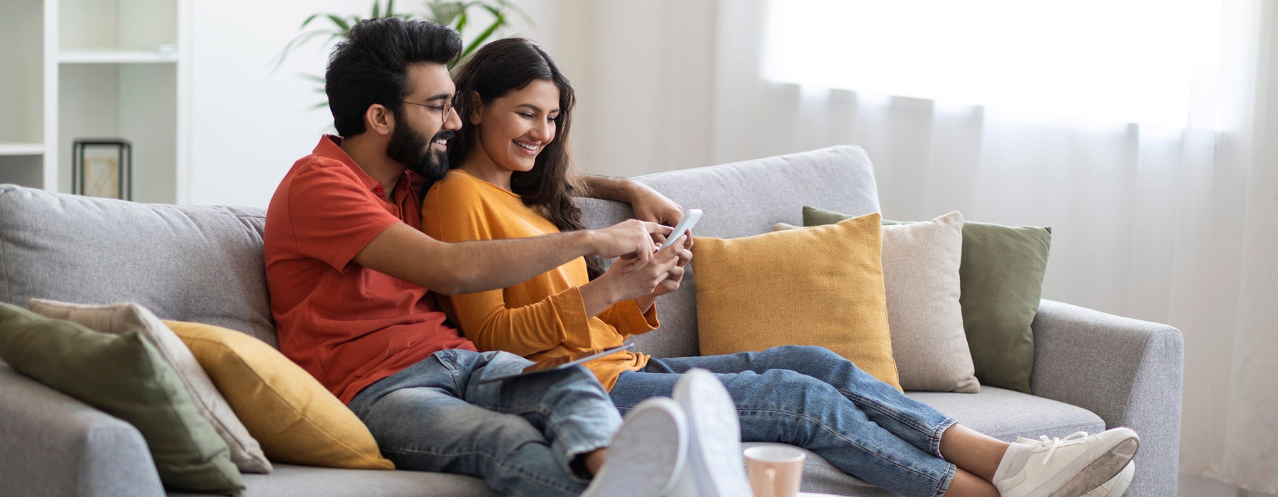 a man and woman sit on their couch and look at a phone