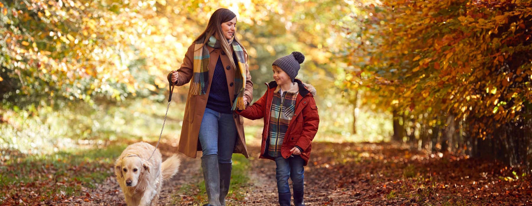 mother and son walking their dog on a trail with trees